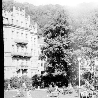 Historic park with grand building, monument, and early 20th-century visitors.