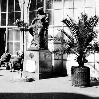 Statue fountain in front of modern building with people resting.