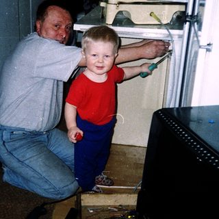 A man kneels helping a young child open a refrigerator.