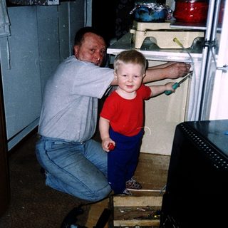 A man kneels helping a young child open a refrigerator.