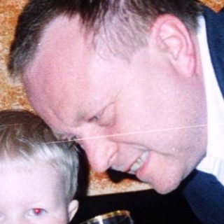 A man in suit playfully drinks from a child's cup.
