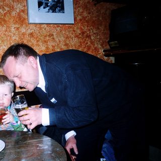 A man in suit playfully drinks from a child's cup.