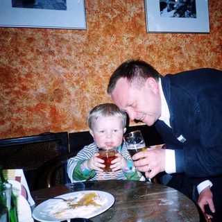 A man in suit playfully drinks from a child's cup.