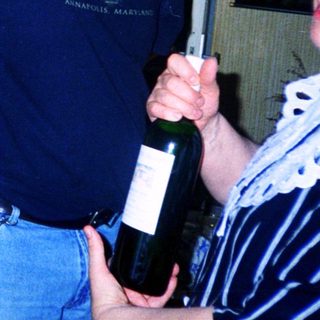 Two adults playfully holding and posing with a wine bottle.