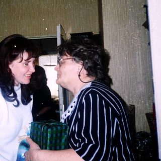 Two women exchanging a wrapped gift indoors.