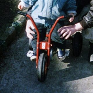 Child learning to ride a bike with adult assistance.