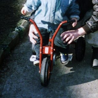 Child learning to ride a bike with adult assistance.