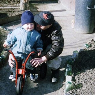 Child learning to ride a bike with adult assistance.