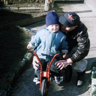Child learning to ride a bike with adult assistance.