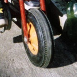 A woman assists a young child riding a red balance bike outdoors.