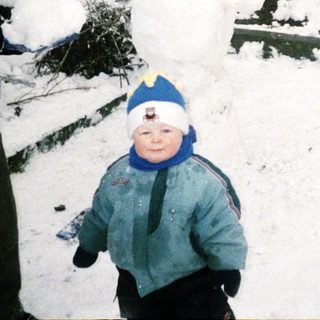 Snowman building with children and adult in snowy yard.