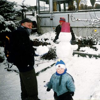 Snowman building with children and adult in snowy yard.
