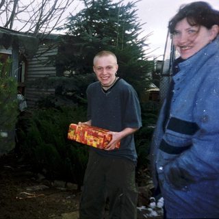Two people standing outside with Christmas tree and gift.