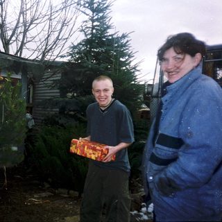 Two people standing outside with Christmas tree and gift.