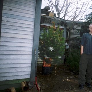 Two people standing beside a burning Christmas tree.