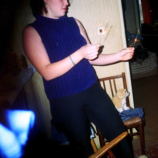 Pregnant woman lighting sparklers with toddler and cat nearby.