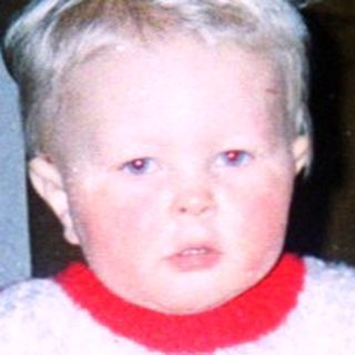Young child riding red toy car indoors.
