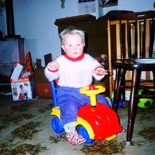 Young child riding red toy car indoors.