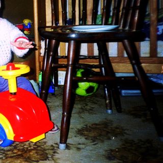 Young child riding red toy car indoors.