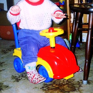 Young child riding red toy car indoors.