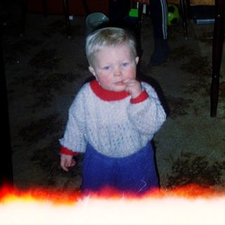 Child standing indoors near woman in dark room.