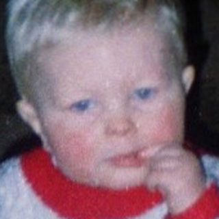 Child standing indoors near woman in dark room.
