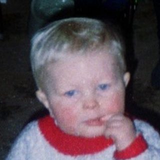 Child standing indoors near woman in dark room.