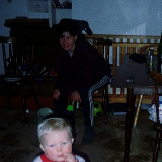 Child standing indoors near woman in dark room.