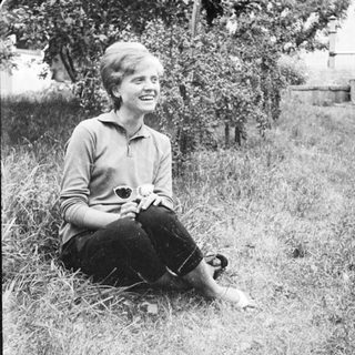 Young woman smiling while sitting in grass outdoors.