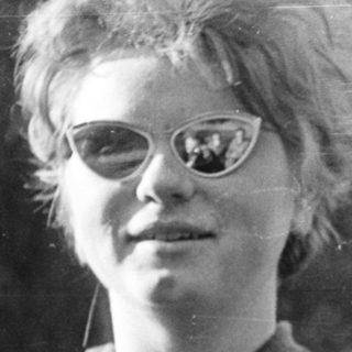Young person with spiky hair wearing glasses outdoors.