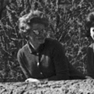 Three individuals leaning on a stone wall in a forested area.