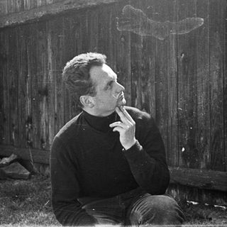 Man smoking outdoors near dilapidated wooden fence.