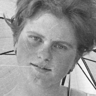 A woman in vintage clothing holds an open umbrella outdoors.