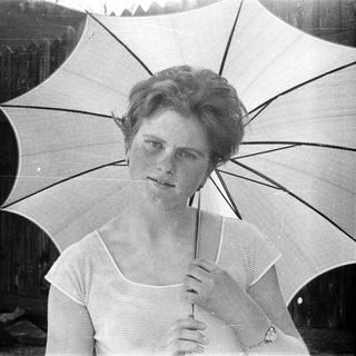 A woman in vintage clothing holds an open umbrella outdoors.