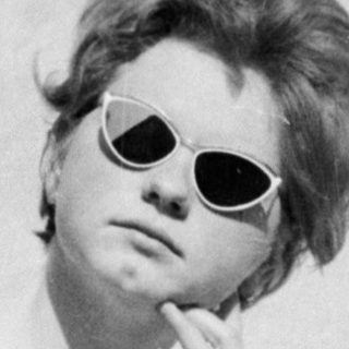 A woman in sunglasses sitting thoughtfully against a wall.