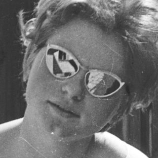 Young woman wearing sunglasses indoors near wooden wall.