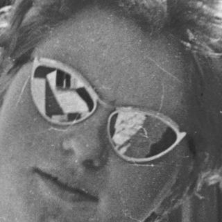 Young woman wearing sunglasses indoors near wooden wall.