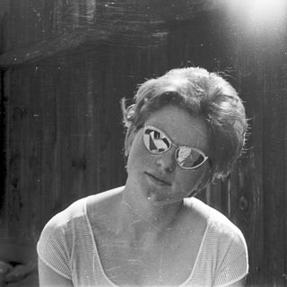 Young woman wearing sunglasses indoors near wooden wall.