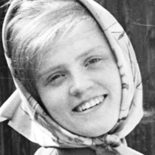 Young girl wearing headscarf and sweater, smiling outdoors.