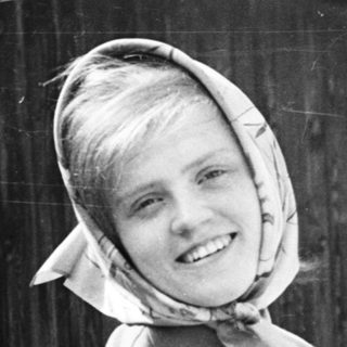 Young girl wearing headscarf and sweater, smiling outdoors.