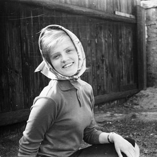 Young girl wearing headscarf and sweater, smiling outdoors.