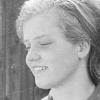 Young woman smiling outdoors near brick wall.