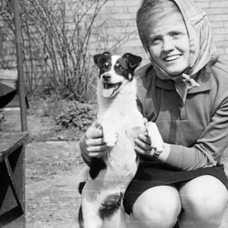Woman kneeling with small dog outdoors.
