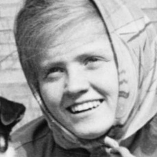 Woman kneeling with small dog outdoors.