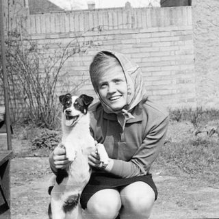 Woman kneeling with small dog outdoors.