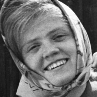 Smiling person adjusting headscarf outdoors.