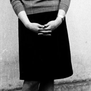Young woman standing outdoors in 1960s-style clothing.