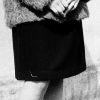 Young woman wearing cardigan and skirt, standing outdoors.