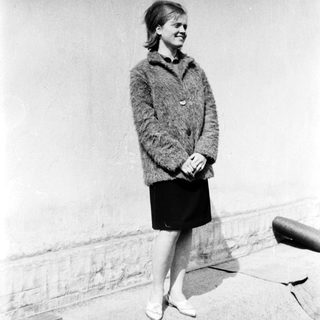Young woman wearing cardigan and skirt, standing outdoors.