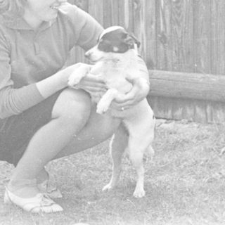 A young girl kneeling, holding a small dog outdoors.